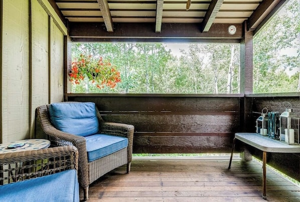 A covered porch with wicker furniture, a table with candles, and a view of trees. - Lovely condo with fireplace, skiing, balcony, full kitchen & washer/dryer (Wilson)