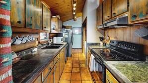 A rustic kitchen with wooden cabinets, a stove, and a tiled floor. - Dog-friendly waterfront cabin on Flat Creek with wood stove, creek view, firepit (Jackson)