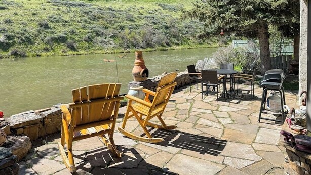 A patio with stone flooring, wooden rocking chairs, a grill, and a view of a river. - Dog-friendly waterfront cabin on Flat Creek with wood stove, creek view, firepit (Jackson)