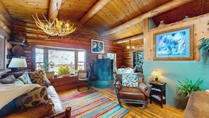 A log cabin interior with a fireplace, wooden furniture, and a chandelier. - Dog-friendly waterfront cabin on Flat Creek with wood stove, creek view, firepit (Jackson)