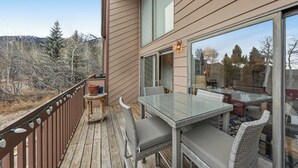 A deck with a glass table and wicker chairs, overlooking a forested area.