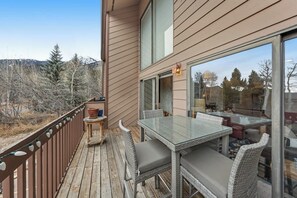 Een terras met een glazen tafel en rieten stoelen, met uitzicht op een bebost gebied.