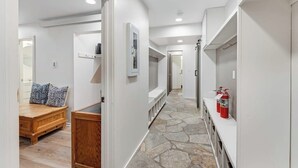 A hallway with a stone floor, white walls, a wooden bench, and a fire extinguisher.