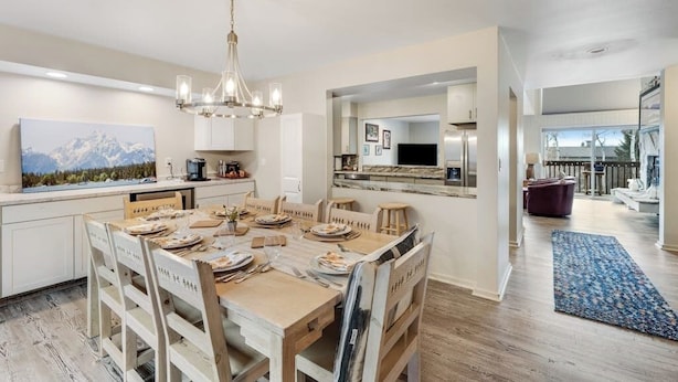 A modern kitchen with a dining area, wooden flooring, and a chandelier.
