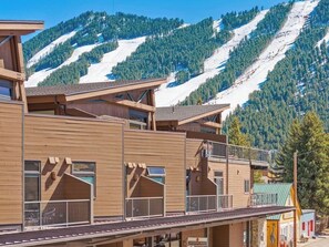 Ein Holzhaus mit Balkonen, im Hintergrund eine Skipiste und ein Schild mit der Aufschrift 'Jackson Hole'.