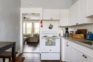 Una cocina compacta con armarios blancos, una estufa y una encimera con varios objetos.