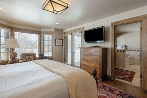 A bedroom with a bed, dresser, television, and a bathroom visible through an open door. - Impressive mtn-view home near national parks with deck, fireplace, & streaming (Jackson)
