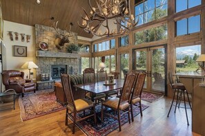 A spacious living room with a large wooden dining table, leather chairs, a stone fireplace, and a deer head mounted above it. - Impressive mtn-view home near national parks with deck, fireplace, & streaming (Jackson)