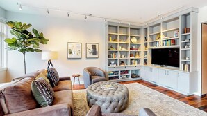 Ein Wohnzimmer mit einer Couch, einem Hocker und einem großen Bücherregal.
