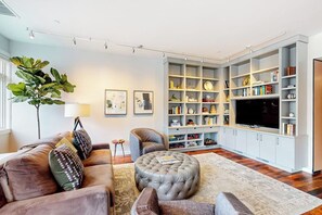 Ein Wohnzimmer mit einer Couch, einem Hocker und einem großen Bücherregal.