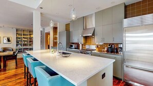Eine moderne Küche mit Kochinsel, Edelstahlgeräten und blauen Barhocker.