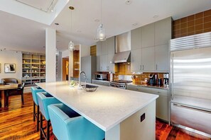 Eine moderne Küche mit Kochinsel, Edelstahlgeräten und blauen Barhocker.