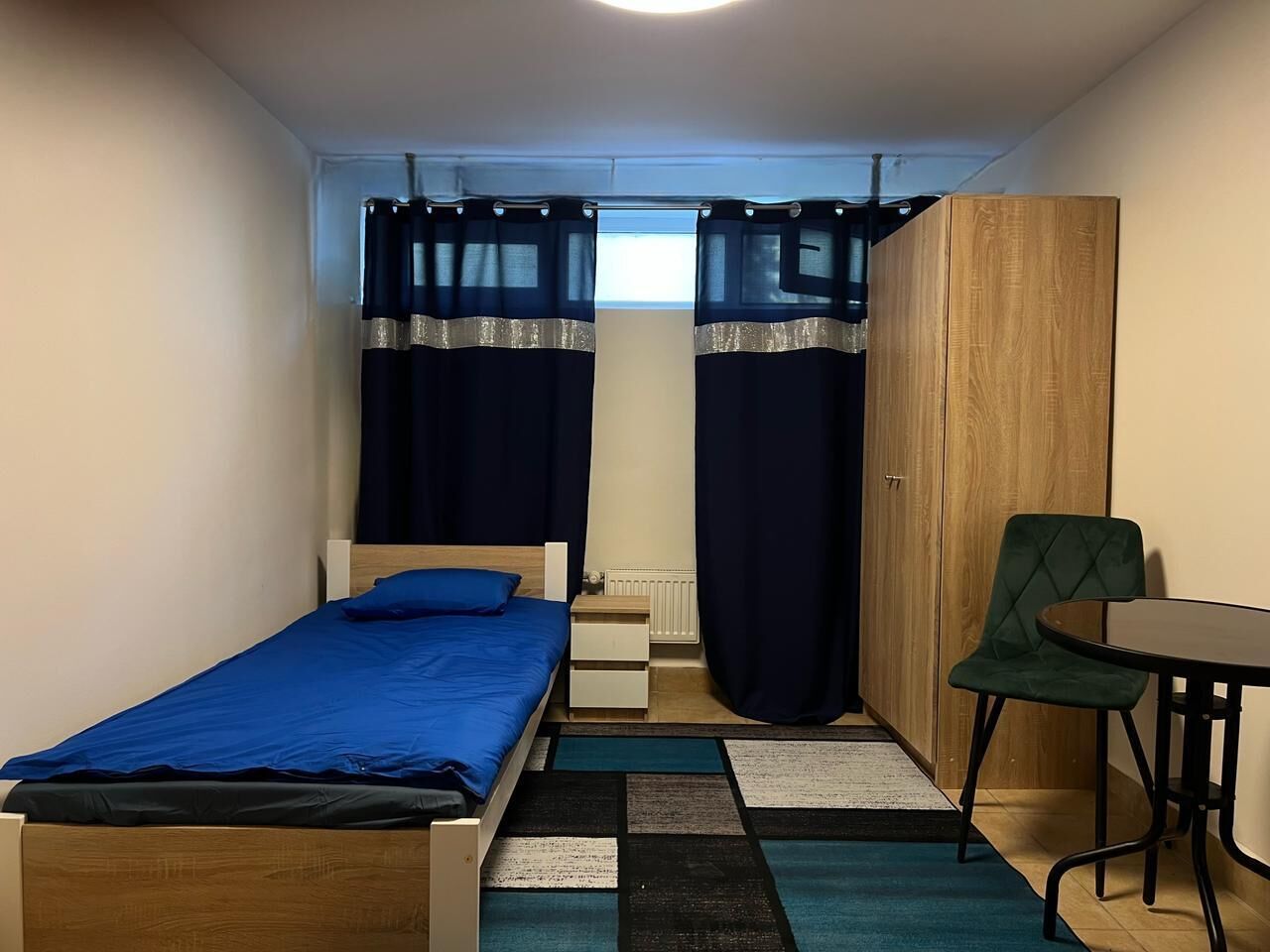 A small bedroom with a single bed, a chair, a table, and a wardrobe.
