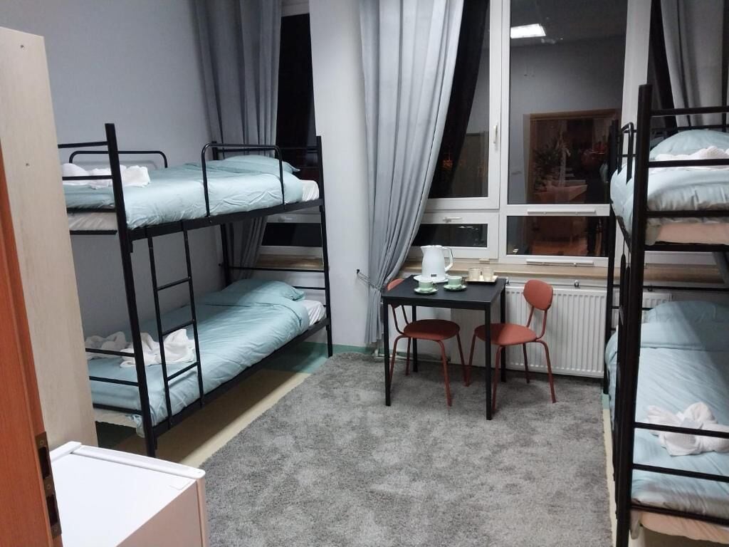 Un dormitorio con literas, una mesita con sillas y una ventana con cortinas.