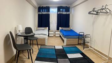 A small, well-lit room with a bed, two bedside tables, a chair, a desk, and a hanging clothes rack.