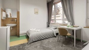 Un dormitorio con cama, escritorio, silla, ventana con cortinas, lavamanos y espejo.