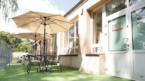 Un patio al aire libre con mesa y sillas, un paraguas grande y un edificio con un letrero.