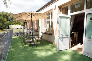 An outdoor patio with tables and chairs, a large umbrella, and a building entrance. - ALLIANCE - M (Warsaw)