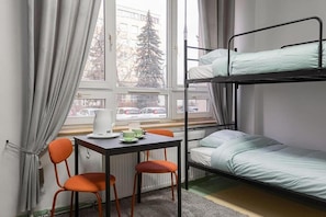 A dormitory room with bunk beds, a table with chairs, a kettle, and a view of a snowy tree outside the window. - ALLIANCE - M (Warsaw)