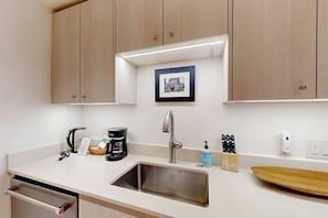 Eine Küche mit einem Edelstahl-Spülbecken, Holzschränken, einer Kaffeemaschine, einem Messerblock und einem gerahmten Bild an der Wand.