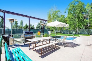 Eine Terrasse im Freien mit Grill, Picknicktischen, einem Pool und einer überdachten Sitzgruppe.