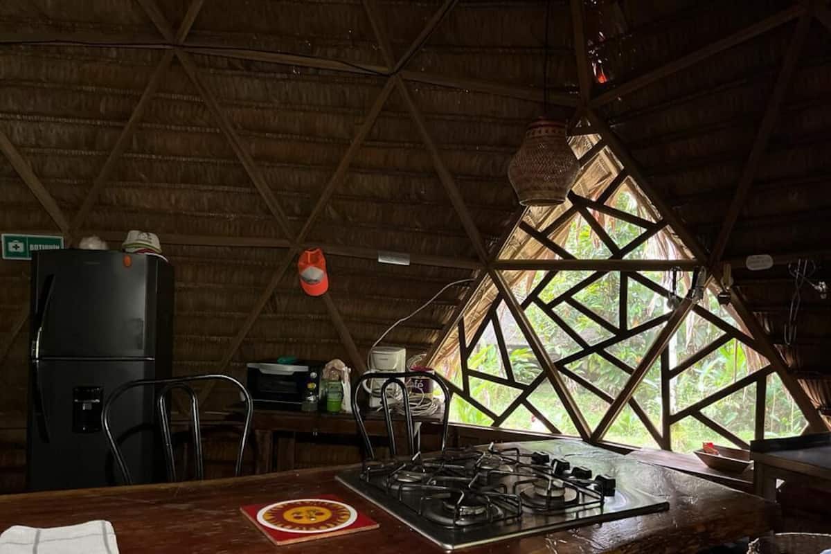 Una cocina con estufa a gas, refrigerador y ventana con diseño geométrico.