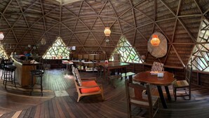 Un intérieur spacieux et décloisonné, avec un plafond haut aux motifs géométriques, un plancher en bois et un bar central.