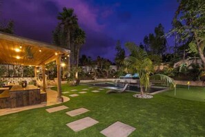 Un patio trasero bien cuidado con piscina, un área de estar techada y un sendero de piedra.