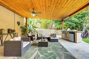 An outdoor patio with wicker furniture, a stone wall, and a grill area.