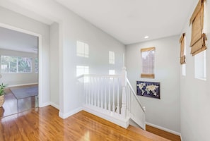 A staircase with white balusters leading to a landing, a world map artwork on the wall, and a potted plant.