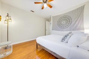 A bedroom with a bed, a ceiling fan, a tapestry, and a floor lamp.