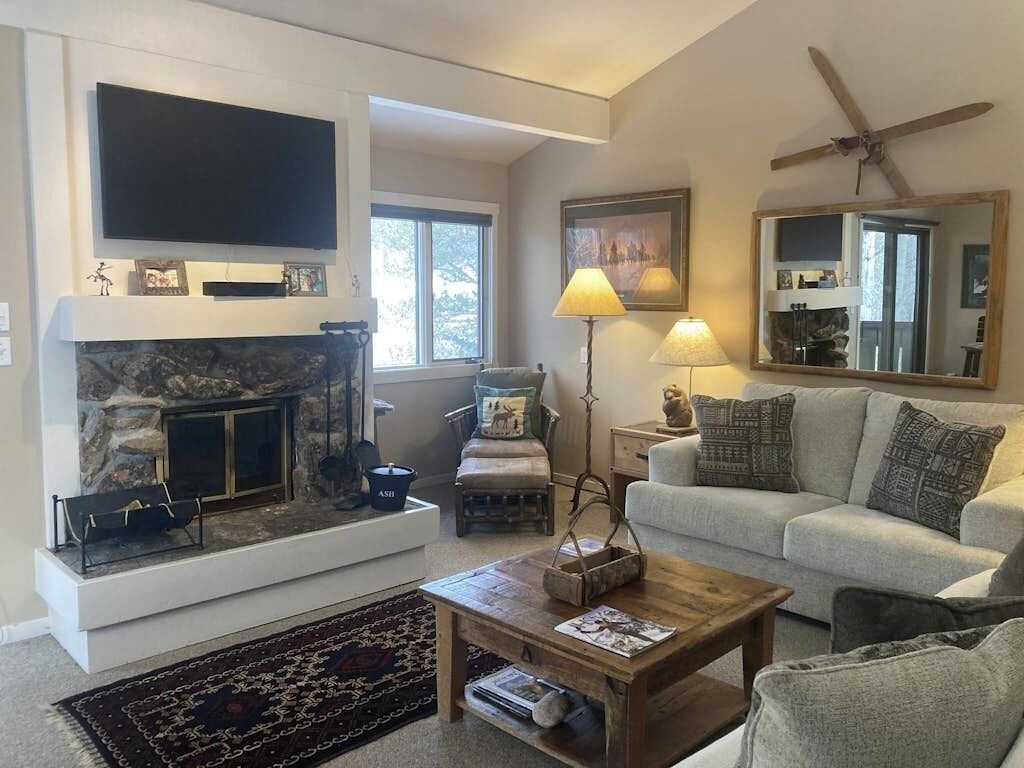 A living room with a fireplace, a sofa, a coffee table, a television, and a ceiling fan.