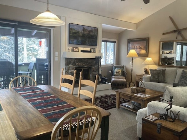 A cozy living room with a fireplace, dining area, and seating. - Riverrfont corner condo with patio, fireplace, electric grill, & washer/dryer (Wilson)