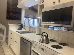 A kitchen with white cabinets, a stove, a kettle, and a window. - Riverrfont corner condo with patio, fireplace, electric grill, & washer/dryer (Wilson)