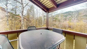 Ein überdachter Außenbereich mit Tisch und Stühlen, umgeben von einem Holmgitter, mit Blick auf eine bewaldete Landschaft.