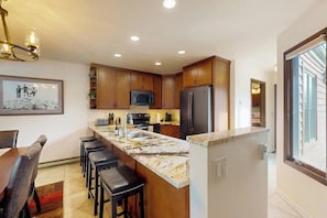 A modern kitchen with wooden cabinets, a marble countertop, and a stainless steel refrigerator.