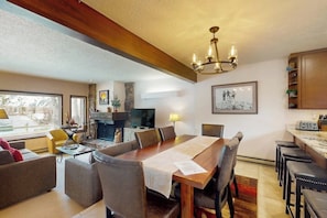 A dining area with a wooden table, chairs, a chandelier, and a fireplace.
