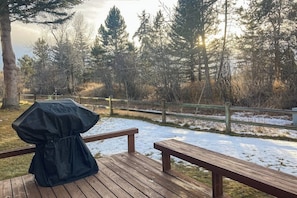 A wooden deck with a barbecue grill and picnic table, surrounded by a wooden fence and trees.