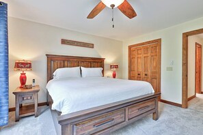 A bedroom with a wooden bed, a ceiling fan, a nightstand with a lamp, and a door with a wooden frame.