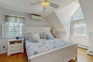A bedroom with a sloped ceiling, a bed with patterned bedding, a nightstand, and a window with shutters. - Bright dog friendly coastal home close to beaches (York)