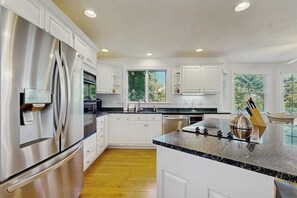 A modern kitchen with stainless steel appliances, white cabinetry, a granite countertop, and a view of greenery outside. - Bright dog friendly coastal home close to beaches (York)