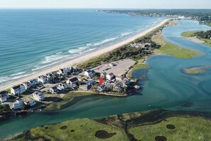 Luftaufnahme einer Küstenimmobilie mit Strand, Wasserflächen und einer Ansammlung von Häusern.