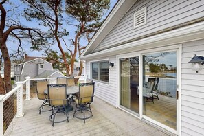 Eine überdachte Terrasse mit Tisch und Stühlen, eine Schiebetür aus Glas und Blick auf ein Gewässer.
