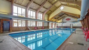 Piscina coperta con soffitto alto, travi in legno e vista su alberi all'esterno.