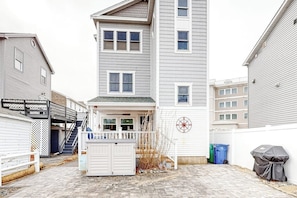 A residential building with a covered porch, a staircase, and a fenced yard. - Comfortable home steps from beach with deck, grill, & washer/dryer (Hampton)