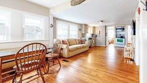 Amplia sala de estar con una mesa de comedor de madera, un sofá y una cocina al fondo.