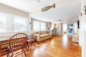 A spacious living area with a wooden dining table, a sofa, and a kitchen in the background. - Comfortable home steps from beach with deck, grill, & washer/dryer (Hampton)