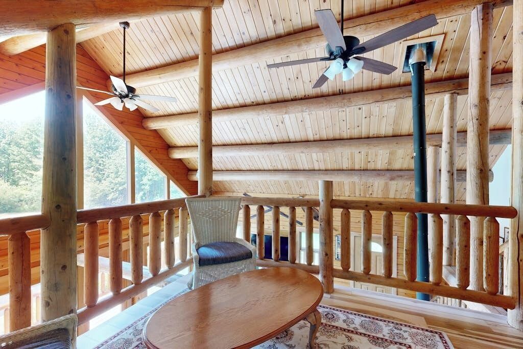 A wooden deck with a table and chairs, ceiling fans, and a railing.