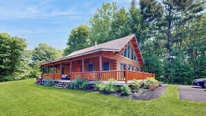 Une cabane en rondins dotée d’un porche, entourée d’une pelouse bien entretenue et d’arbres.