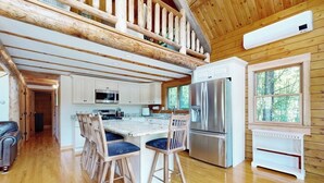 L’intérieur d’une cabane comprend une cuisine, un plancher en bois, un coin repas avec des tabourets de bar et une chambre à l’étage avec un plafond en bois.